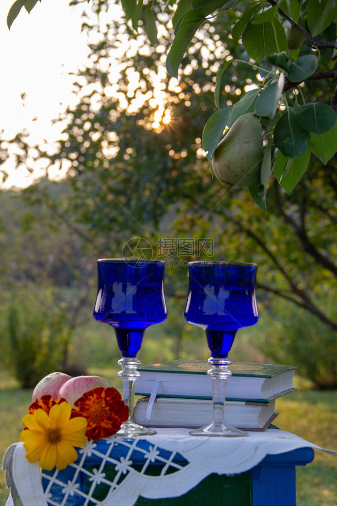 两个玻璃蓝色玻璃杯两本书一个苹果和鲜花站在用桌布装饰的凳子上图片