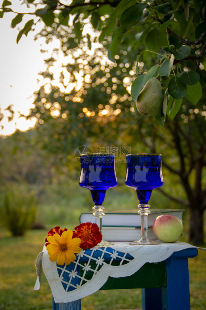 两个玻璃蓝色玻璃杯两本书一个苹果和一个用桌布装饰的凳子上的花图片