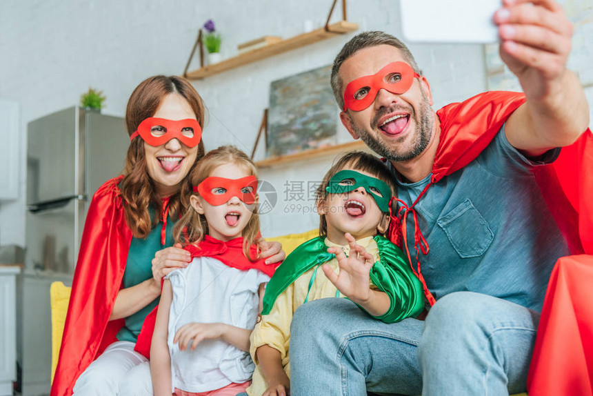 在超级英雄服装中快乐家庭有选择焦点在家里用智能手机自拍时用图片
