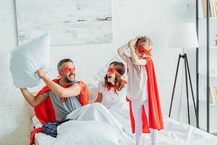 快乐的父亲穿着超级英雄的装扮抱着枕头坐在妻子和女儿图片
