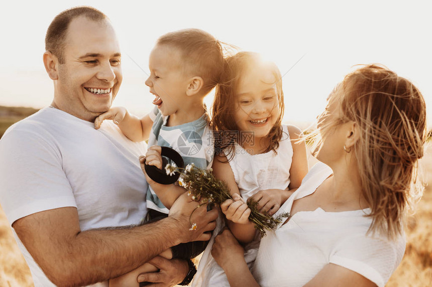 一个可爱的年轻家庭在母亲和父亲怀里抱着他们的女儿和子对抗日落图片
