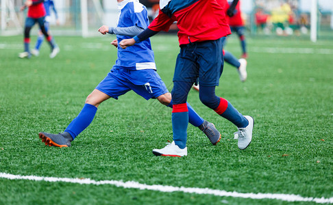 穿着红色和蓝色运动服的男孩在球场上踢足球图片