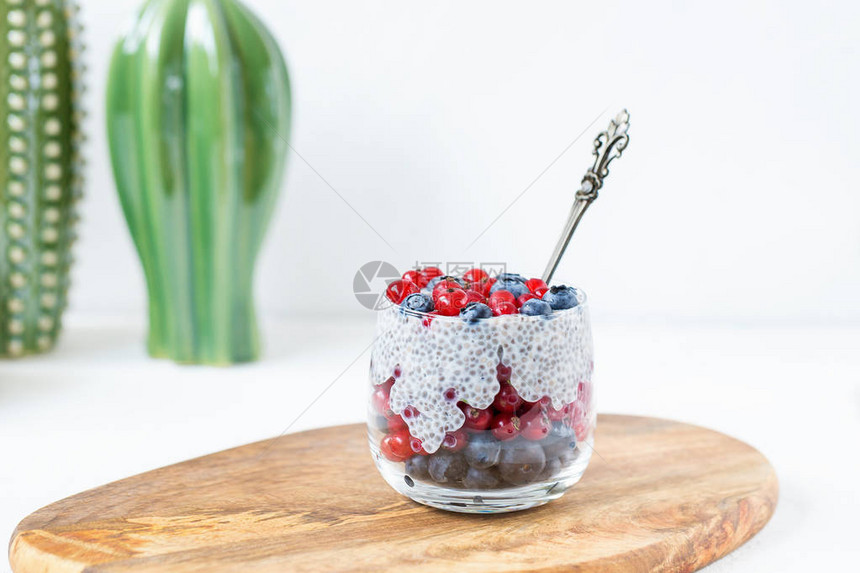 配有新鲜蓝莓的Chia种子布丁一杯红草莓和木板上的勺子超级食物和素食品概图片