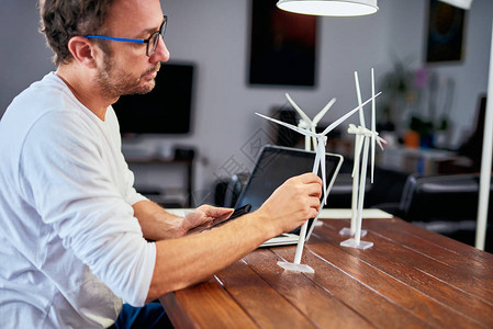 英俊的白种人生态工程师坐在家里拿着风车模型桌上是风车模型可图片