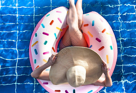 戴帽子的女人在蓝色水池中以甜圈的形式在充气圆圈上放松从顶部的视图夏图片