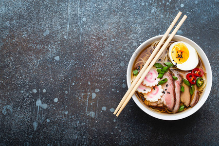 美味的日本面条汤拉面在白色陶瓷碗肉汤猪肉片火影忍者蛋黄质朴的石头背景上背景图片