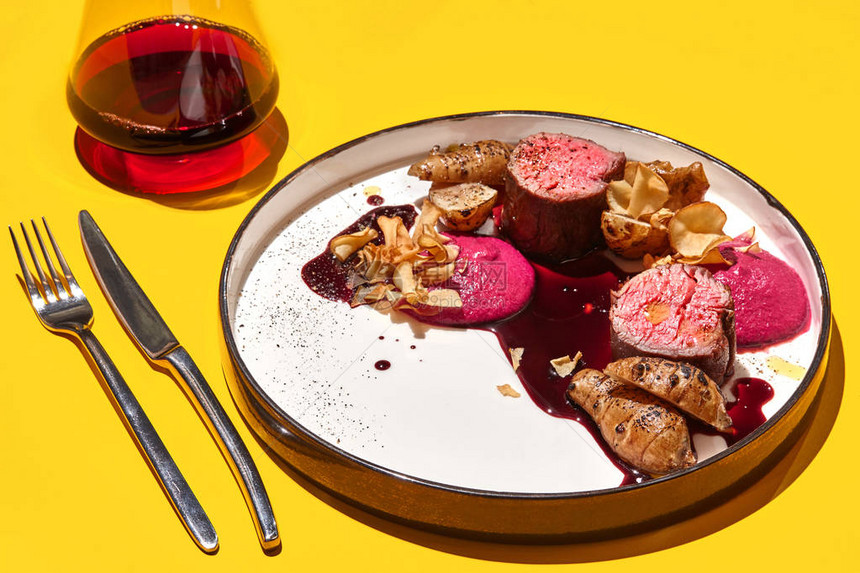 在白盘上盛着黑面粉和一杯红葡萄酒刀和叉子黄桌图片