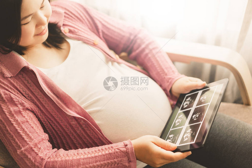 孕妇在照顾孩子的同时在家感到快乐年轻的准妈在数字平板电脑上看怀孕的照片产前护理和图片
