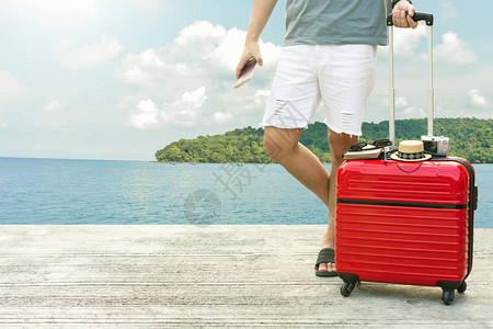 在模糊的城市背景下手持红色行李箱和护照的男子图片