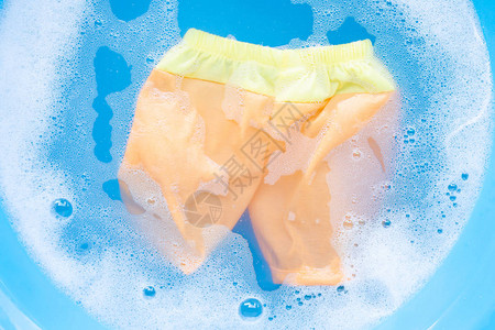 黄色和橙色婴儿短裤浸泡在婴儿洗衣粉水溶解洗衣布蓝色背景图片