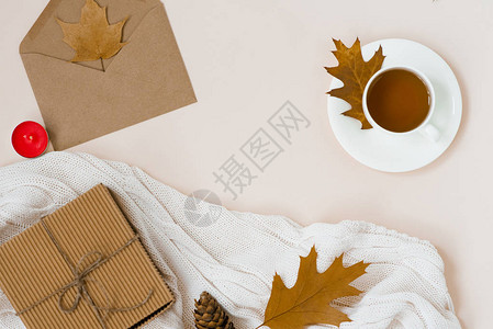 秋平铺着白色针织格子热茶和落棕叶蟹包礼盒米色浅背景上的顶级静物秋季概图片
