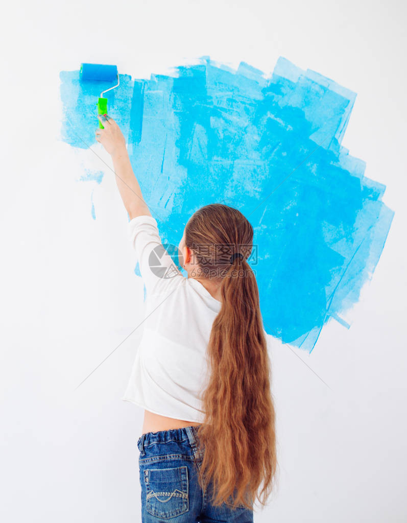 女快乐女孩用蓝油漆在墙上涂彩图片