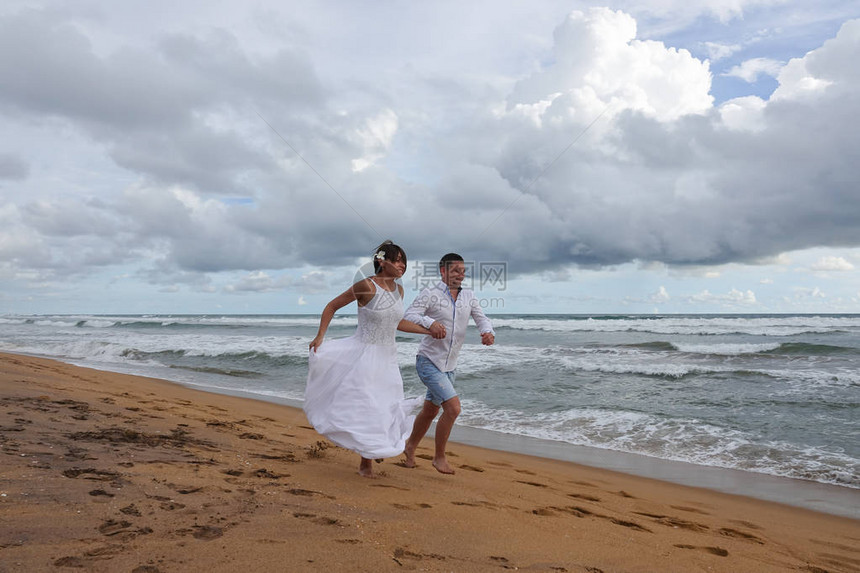 年轻夫妇在热带海滩上手牵跑来去图片