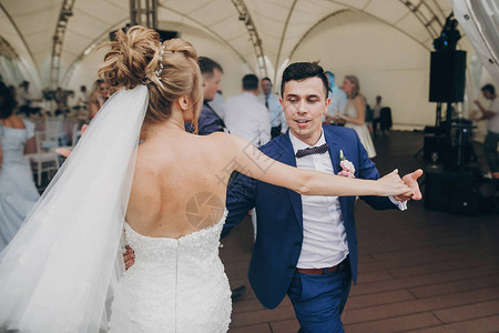 时尚快乐的新娘和新郎在婚宴上玩乐和跳舞华丽的新婚夫妇在客人的背景图片