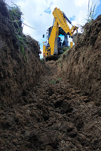 一座黄色挖土机在建筑工地上挖壕沟图片