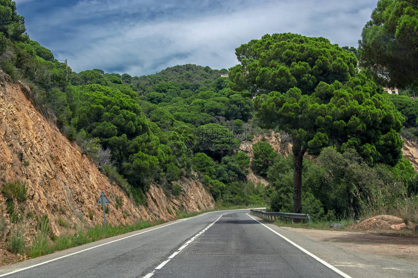 在西班牙加泰罗尼亚的蓝色云层天空下覆盖着绿树的岩石中图片