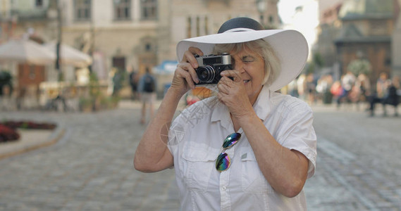 高级女游客在乌克兰利沃夫旅行时探索小镇并用复古相机拍照戴帽子的优雅女图片
