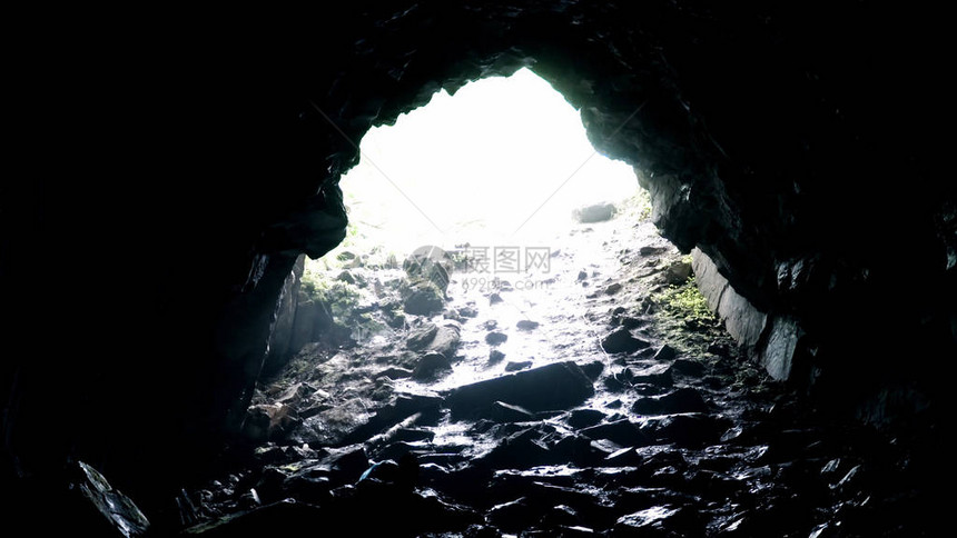 从黑暗的岩石洞穴中退出影视素材岩石洞穴出口处的明亮光线在潮湿中被黑暗覆盖阴天洞穴中图片