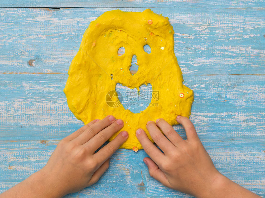 这孩子在木制桌子上画了黄色黏液的滑稽脸孔玩具抗压剂发展手动运图片