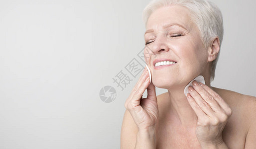 享受美貌和日常面部护理用棉垫清洗皮肤的有吸引力的老年妇女图片