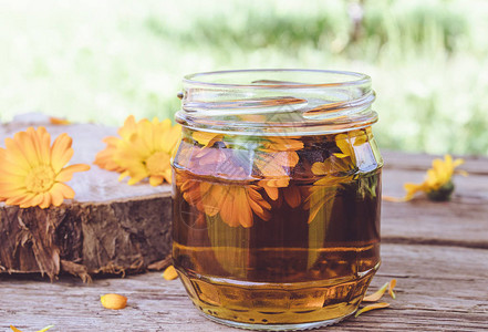 金盏花的酊剂提取物与鲜花在玻璃罐在自然的木制背景上金盏花酊的提取图片