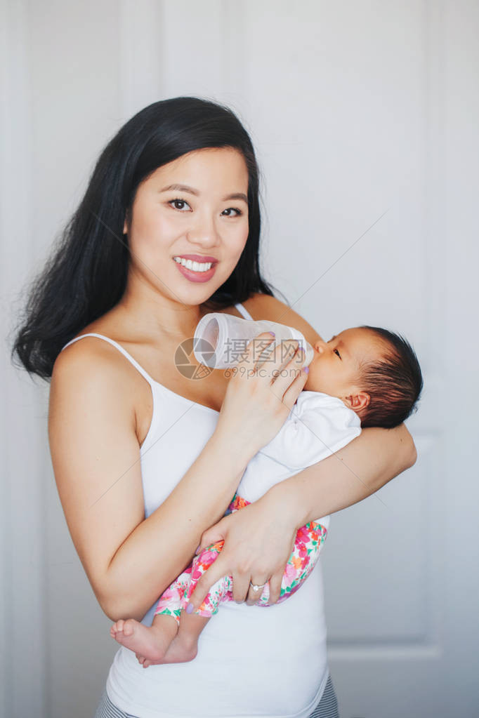 年轻的亚洲母亲用瓶子里的配方奶粉喂养刚出生的小儿子女儿的画像真实的生活方式坦诚真实的时刻真正的母图片