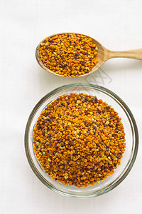 蜂花粉颗粒在玻璃碗和白色背景上的木勺超级食品花蜜酶蜂蜜和蜡营养素氨基酸脂质和维生素Flatlay背景图片