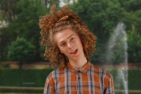 一个卷发年轻男子的肖像满头发的木梳子在公园背景中微笑图片