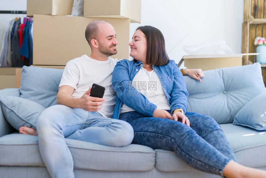 坐在新家沙发上的小情侣使用智能手机图片