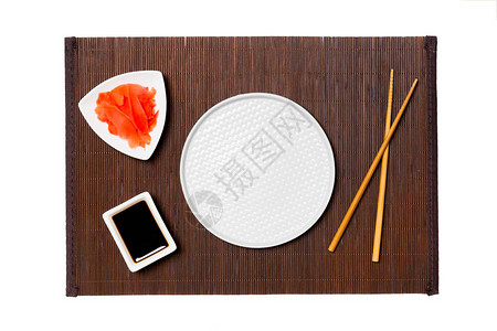 深色竹席背景上用筷子盛放寿司生姜和酱油的空圆白盘为您设计的带有复制图片