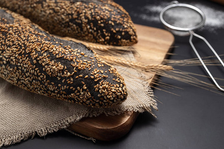 黑色背景的老式毛巾上的自制酸面包法式长棍面包图片