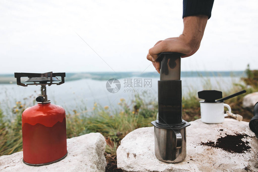 旅行者在湖边悬崖上的aeropress中通过咖啡压热水图片