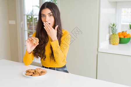 年轻女人在家中吃巧克力薯饼时用手顶着嘴唇吃巧克力饼干图片