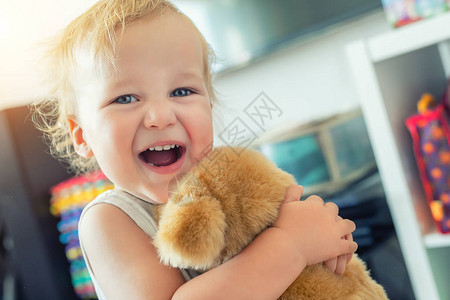 可爱的白种人金发蹒跚学步的男孩在室内玩乐大笑和柔软的小狗玩具格开朗的孩子在家里玩泰迪熊小朋友动物玩具快背景图片