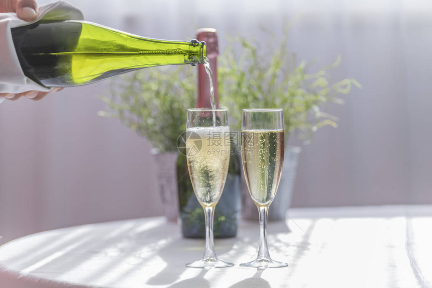 酒保用两副优雅的眼镜提供豪华黄色香槟在背景中喝着一瓶绿色香槟派对和婚礼图片