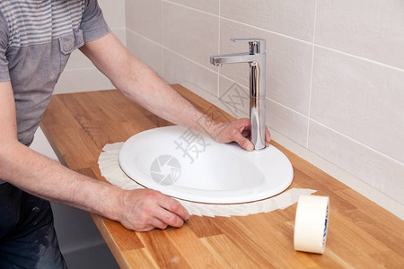 一位专业水管工的特写手在浴室的木桌上安装了一个白色椭圆形陶瓷水槽图片