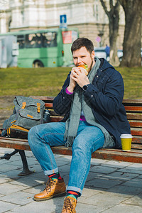 年轻微笑的男子吃汉堡和喝咖啡图片