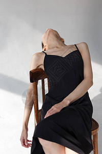 身穿黑色连衣裙的年轻美丽高加索女孩在白色emty天幕上的木椅上摆姿势图片