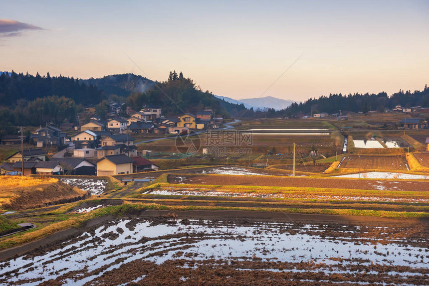 日出时山环绕着山脉的当地房屋和稻田景观图片