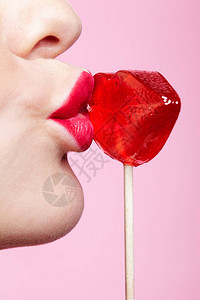 红色女嘴唇形状棒糖女人嘴唇亲吻糖果的特写镜头粉红色背景上的脸部微距照图片