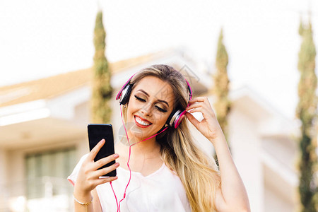 现代年轻女在她的智能手机和耳机上听音乐图片