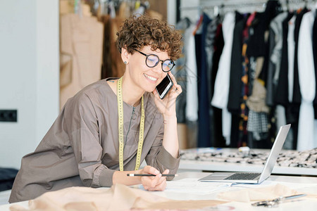 女裁缝用眼镜和便装与客户通过电话交谈时弯曲图片