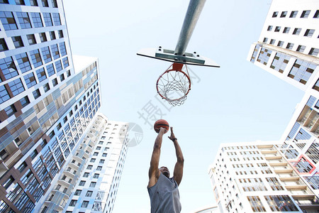 城市背景下非洲篮球运动员在天空中扣篮的低角度动作镜图片