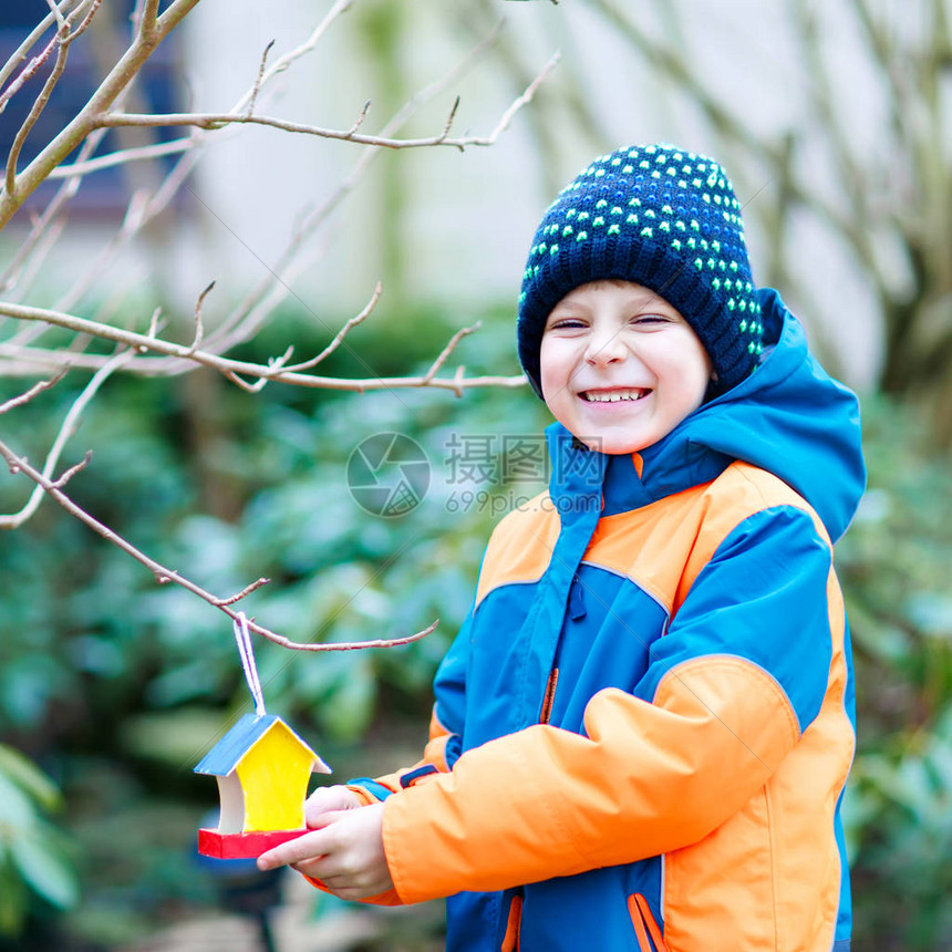 小男孩在冬天喂鸟可爱快乐的学龄前儿童在寒冷的寒冷天把五颜六色的自制鸟屋挂在树上穿着五颜六色的wam衣服的学龄前儿童自然图片