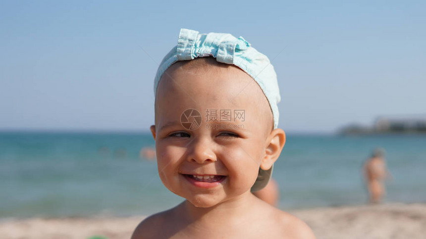 站在海滩上的蓝帽快乐微笑的孩子的特写肖像背图片
