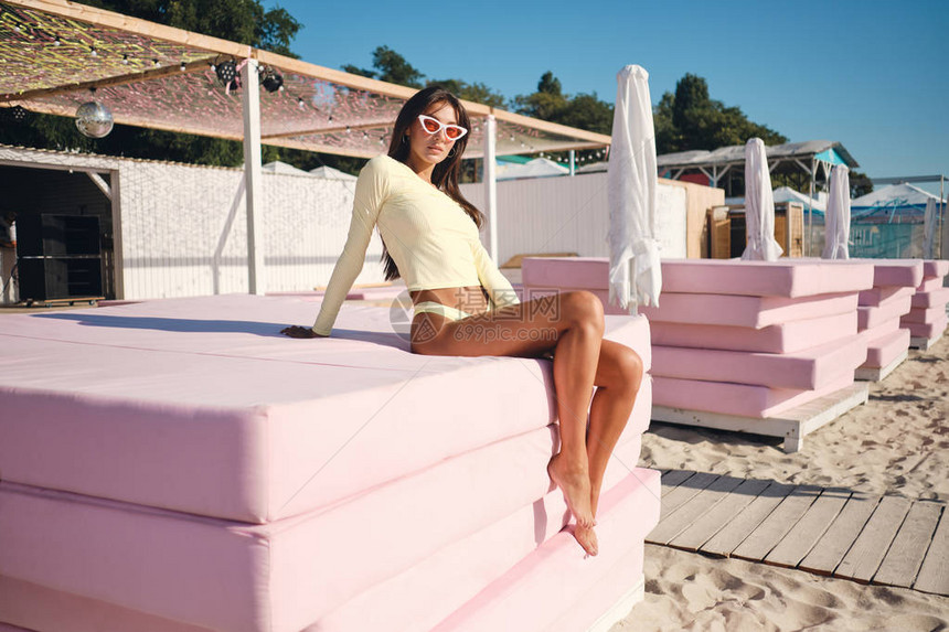 穿着泳装和彩色太阳镜的迷人黑发女孩在海滩粉红色床垫上图片