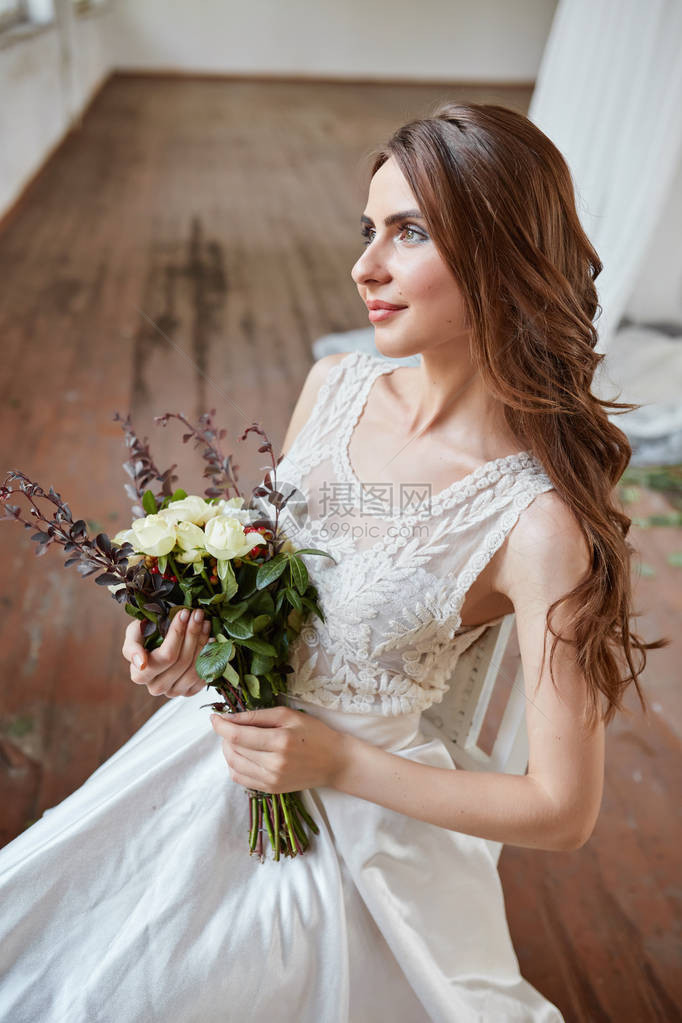 美丽的新娘穿着婚纱在明亮时尚的工作室欧式婚礼装饰和花束在手年轻女孩站着图片