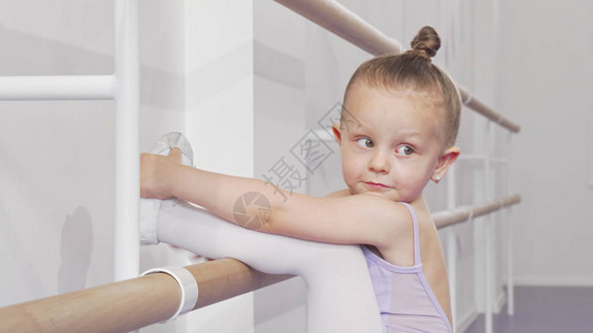 可爱的小芭蕾舞女孩把她的腿放在芭蕾舞杆上伸展图片