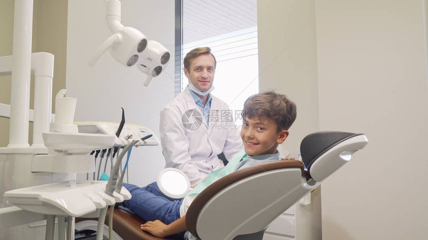 格开朗的小男孩和他的牙医对着镜头微笑成熟的男牙医在体检后与他的小病人交谈牙科诊图片