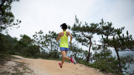 参加运动服装运动的年轻女运动员在森林山道上奔跑图片